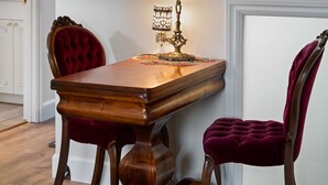 A wooden table with a vintage lamp, two velvet chairs, and a framed picture on the wall. - The Victorian Story at Midtown Manor (Bend)