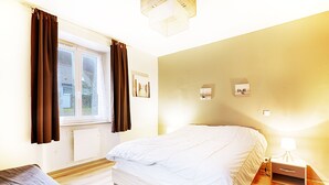 A bedroom with a bed, a nightstand, a window with curtains, and a wall-mounted light fixture.