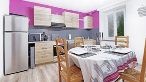 A modern kitchen with wooden cabinets, a stainless steel refrigerator, and a dining area with a table set for four.