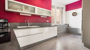 A modern kitchen with white cabinetry, a red accent wall, and a built-in oven. - L'Ostal de Pomérols - Grande maison pour 10 (Pomérols)