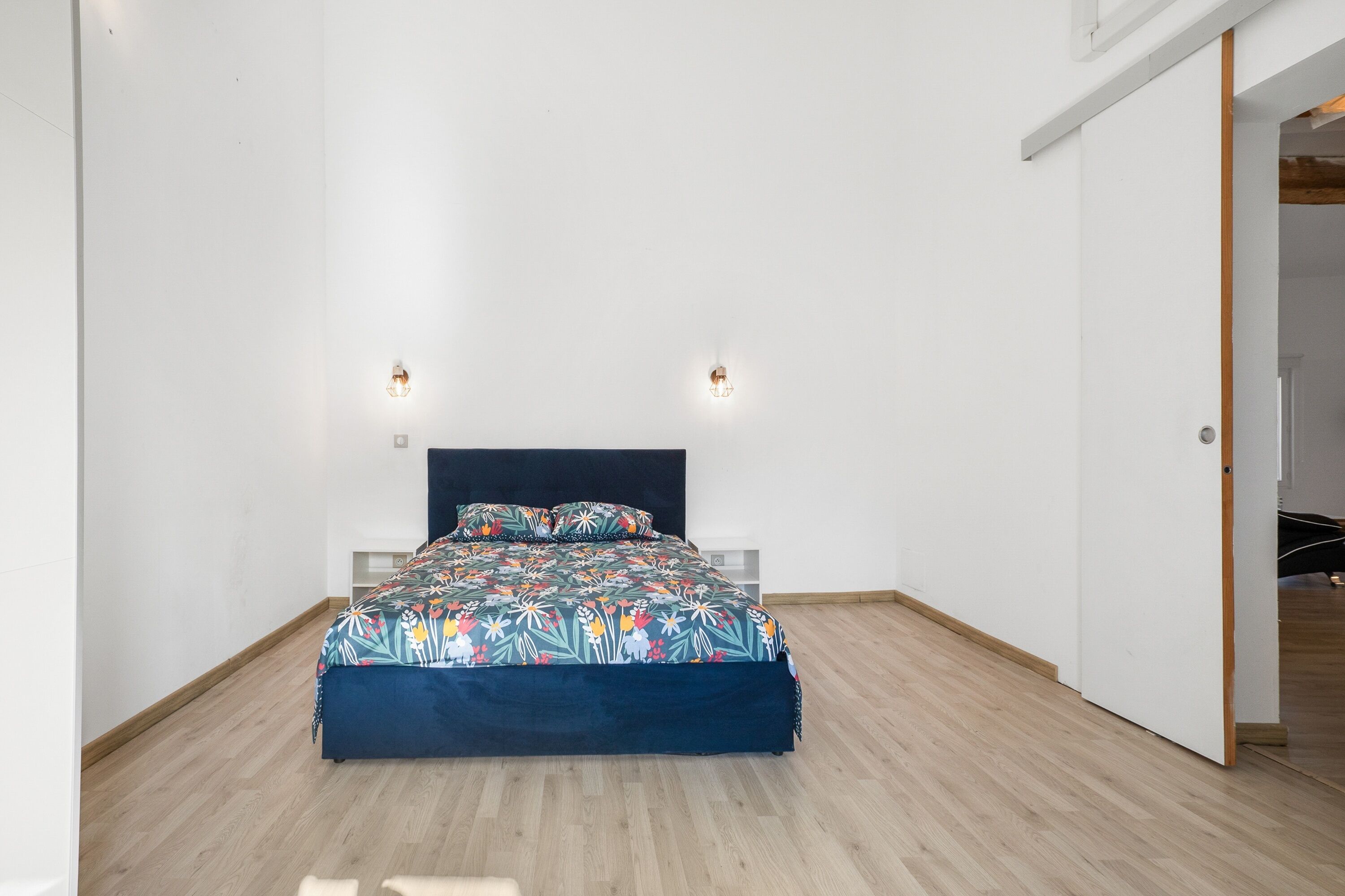 A bedroom with a bed, two wall-mounted lights, and a wooden floor.
