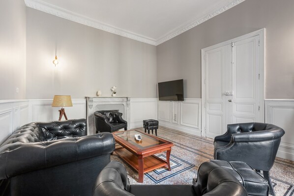 A living room with a leather sofa, a glass coffee table, a television, and a fireplace. - L'Ostal de Pomérols - Grande maison pour 10 (Pomérols)