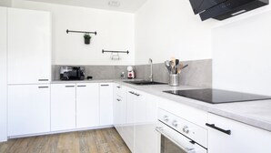Une cuisine moderne avec des meubles blancs, une plaque de cuisson à induction noire, un four encastré et un évier en acier inoxydable.