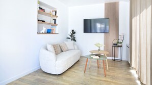 Un salon moderne avec un canapé, une petite table ronde, une bibliothèque et un téléviseur fixé au mur.