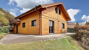 Ein zweistöckiges Holzhaus mit geneigtem Dach, großen Fenstern und einer überdachten Terrasse.