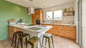 A modern kitchen with a central island, wooden cabinetry, and a large window providing natural light. - Le 101 - Plage du Dossen à Santec à 1.5 km (Santec)