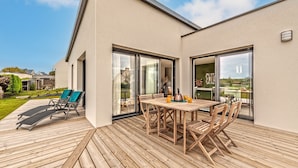A modern outdoor patio with a wooden deck, a table with chairs, and two lounge chairs. - Le 101 - Plage du Dossen à Santec à 1.5 km (Santec)