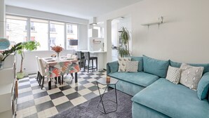 Een moderne woonkamer met een blauwgroene bank, een eethoek met een geruit vloerkleed, en een keuken op de achtergrond.