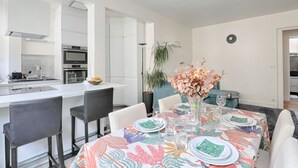 Een moderne keuken met witte kastjes, een ingebouwde oven en een eethoek met een tafel voor vier personen.