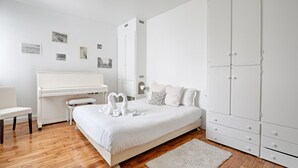 Een moderne slaapkamer met een groot bed, een piano, een bureau en een kledingkast.