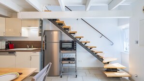 A modern kitchen with a built-in oven, a stainless steel refrigerator, and a wooden staircase with a black railing.