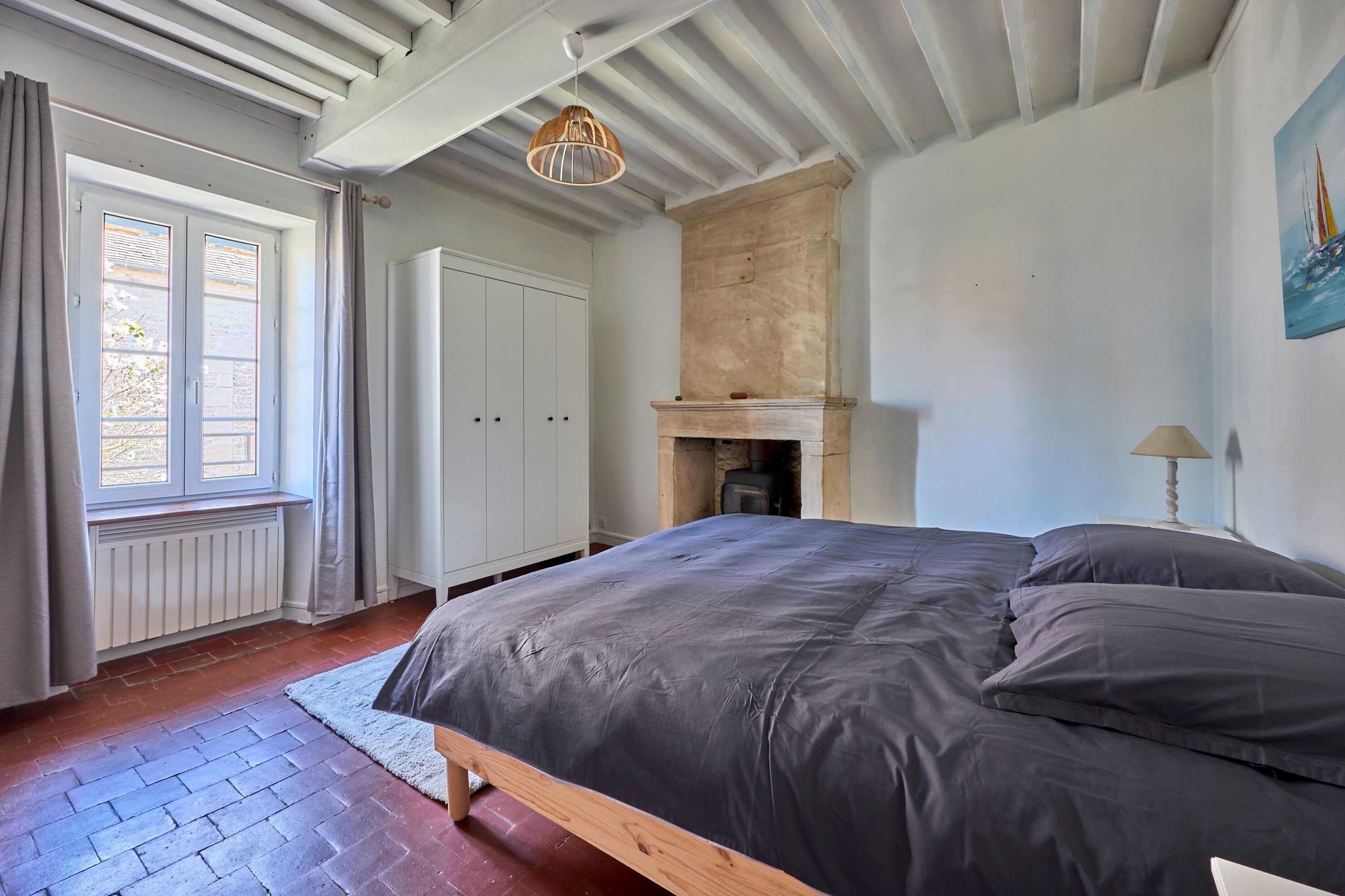 A bedroom with a bed, a fireplace, a window with curtains, and a painting on the wall.