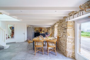 Un comedor con pared de piedra, sillas de mimbre y una mesa preparada para cuatro.