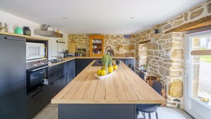 Una cuina moderna amb una illa central, parets de pedra i vistes cap a l'exterior.