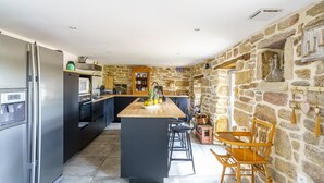 Una cuina amb una illa central, armaris negres, un frigorífic d'acer inoxidable i una paret de pedra.