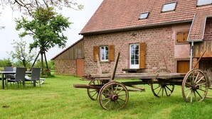 Un edificio de piedra con techo de tejas, un carro de madera y un área de comedor con sillas y una mesa.