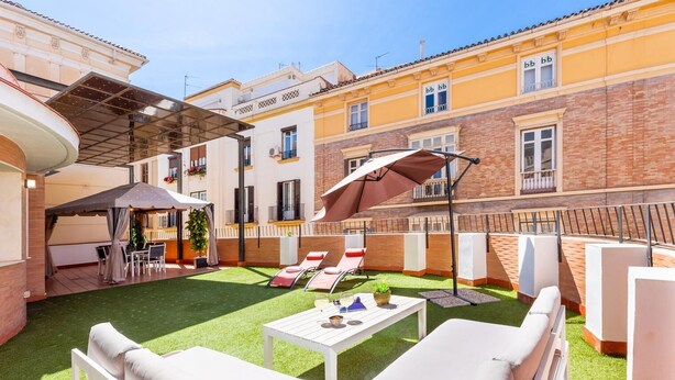 A courtyard with artificial grass, white lounge chairs, a table with drinks, and a covered seating area. - Great private terrace in the heart of the city centre  (Málaga)