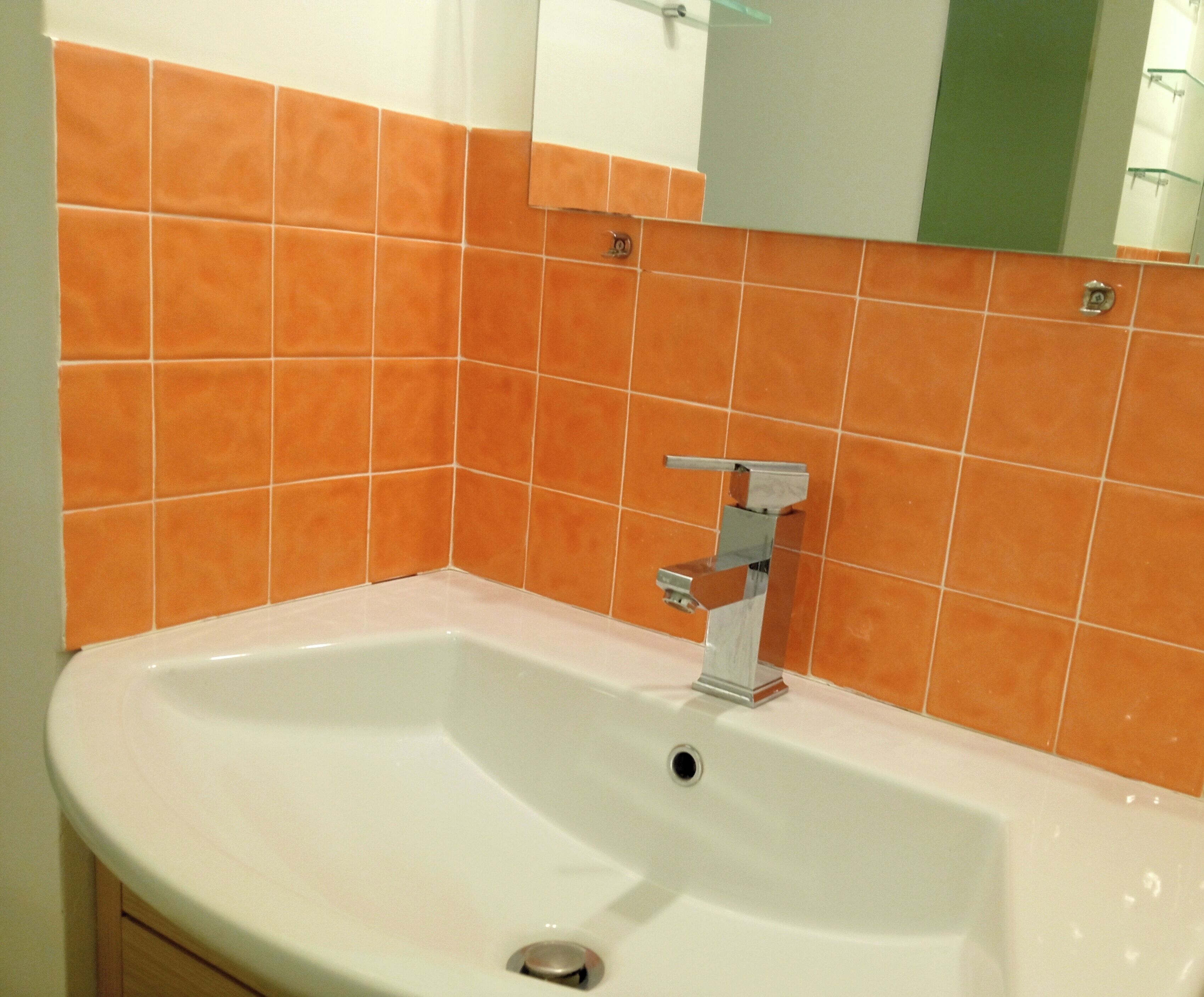 Une salle de bain avec un lavabo blanc, un robinet chromé et des carreaux orange.