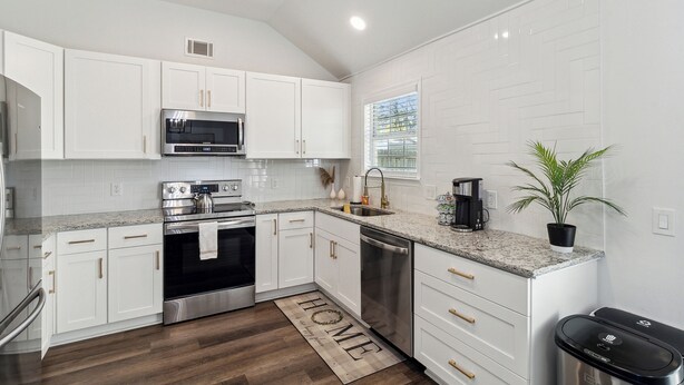 A modern kitchen with white cabinetry, stainless steel appliances, and a wooden floor. - Boho Chic Retreat Savannah/Dog Friendly/3 BD/2 BATH (Savannah)