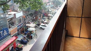 Un balcon donnant sur une rue animée, avec des boutiques et un parasol à rayures bleues.