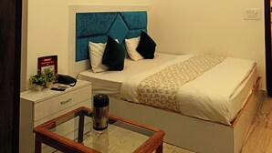 Une chambre à coucher avec un lit, une table de chevet avec un téléphone et une télécommande, un ventilateur de plafond et une petite table de nuit avec une plante.