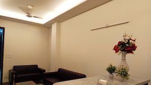 Un espace d’accueil avec un comptoir en marbre, une table basse en verre, un canapé brun foncé et un vase rempli de fleurs rouges.