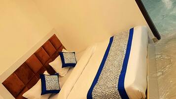 Ein ordentlich bezogenes Bett mit einer blauen und weißen Bettdecke und Kissen, ein Holz-Kopfstück und ein Nachttisch mit einer Lampe.