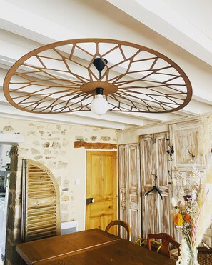 Un coin repas rustique avec une table en bois, un ventilateur de plafond et une porte dotée d’un volet en bois.