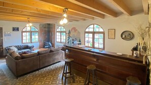 A cozy interior with a wooden ceiling, a bar area with stools, a patterned floor, and a large window. - Maison de Caractère à Saint-nectaire (Saint-Nectaire)