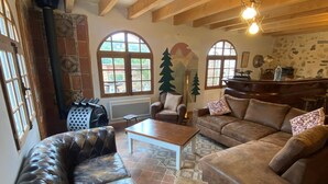 A cozy living room with a leather sofa, a wooden coffee table, and a brown couch. There are large windows with arched tops, a fireplace, and a stone wall with a mountain mural. - Maison de Caractère à Saint-nectaire (Saint-Nectaire)