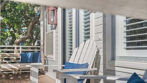 A covered outdoor seating area with white Adirondack chairs and blue cushions, a wooden deck, and a view of a tree and building in the background. - 125 Yards to Private Beach Access. 350 Yards to Gulf Place. Private Pool. LSV. (Santa Rosa Beach)