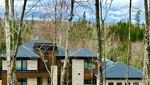 Ein modernes, zweistöckiges Haus mit Natursteinfassade, großen Fenstern und einem geneigten Dach.