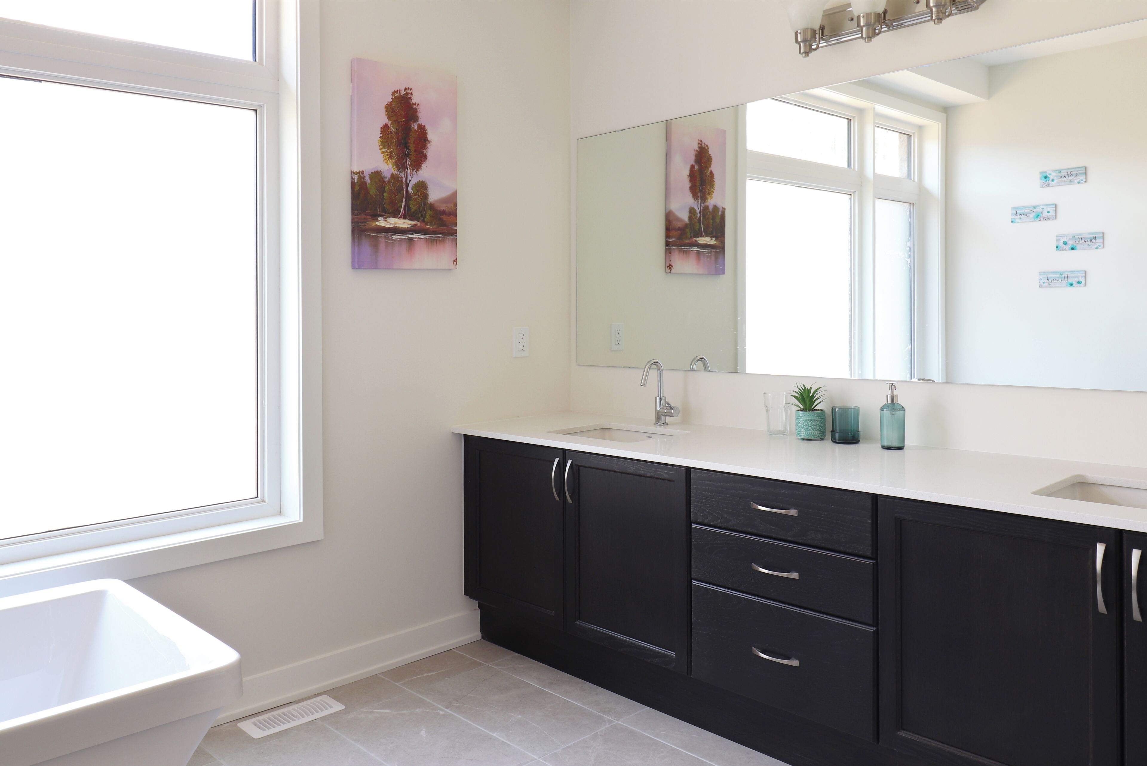 A modern bathroom with a large window, a sink, a mirror, and dark cabinets.