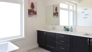 A modern bathroom with a large window, a sink, a mirror, and dark cabinets.