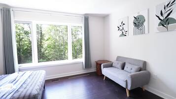 Une chambre moderne avec un lit, un canapé gris, une fenêtre avec des rideaux et trois œuvres d’art accrochées au mur.