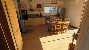 A kitchen with wooden cabinets, a dining table with chairs, a stove, and a window. - New single-storey chalet in Gérardmer (Xonrupt-Longemer)