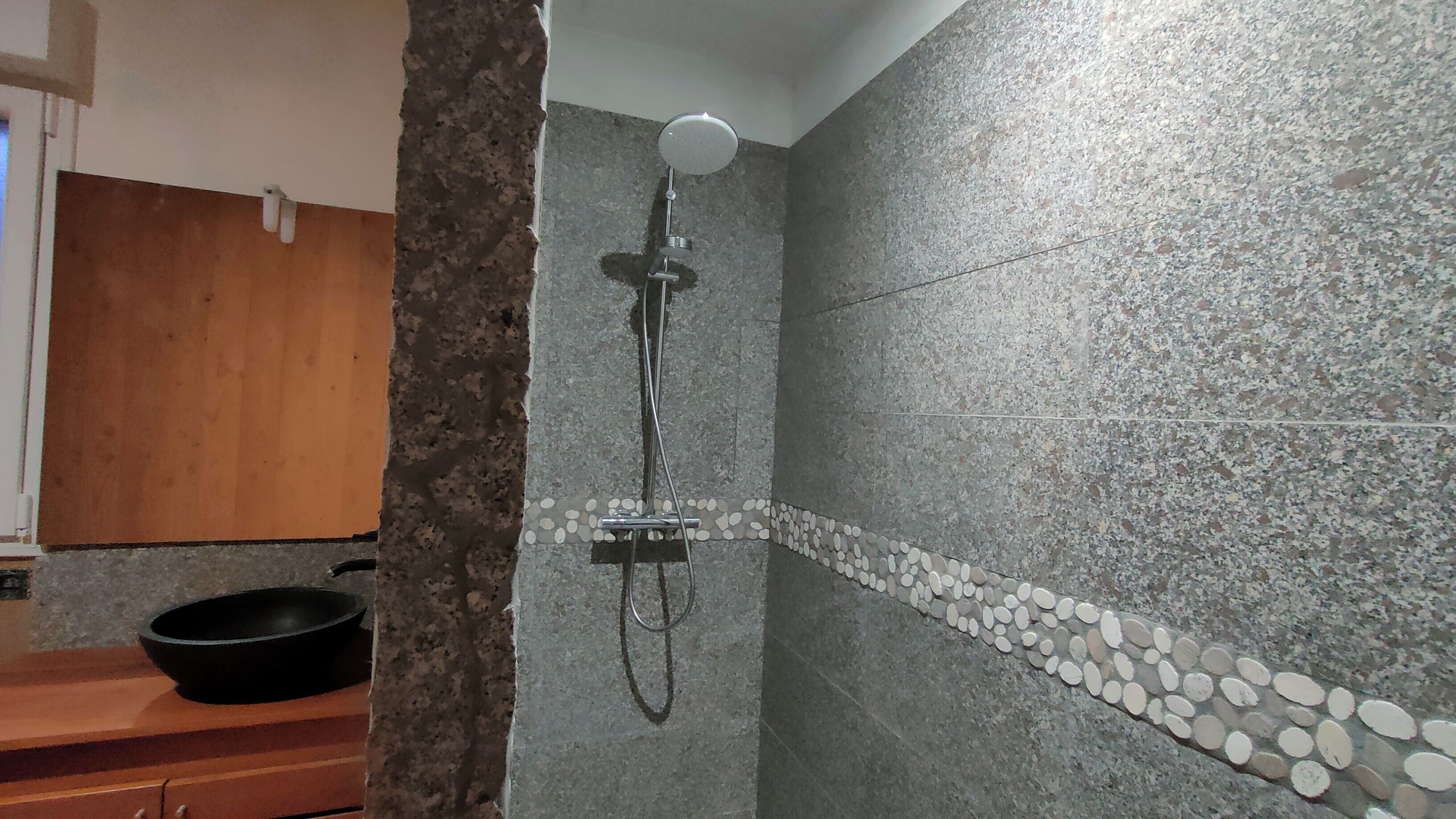 A shower with a handheld showerhead and a wall-mounted faucet.