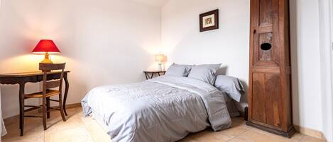 A bedroom with a bed, a desk with a lamp, a wooden cabinet, and a wall clock.