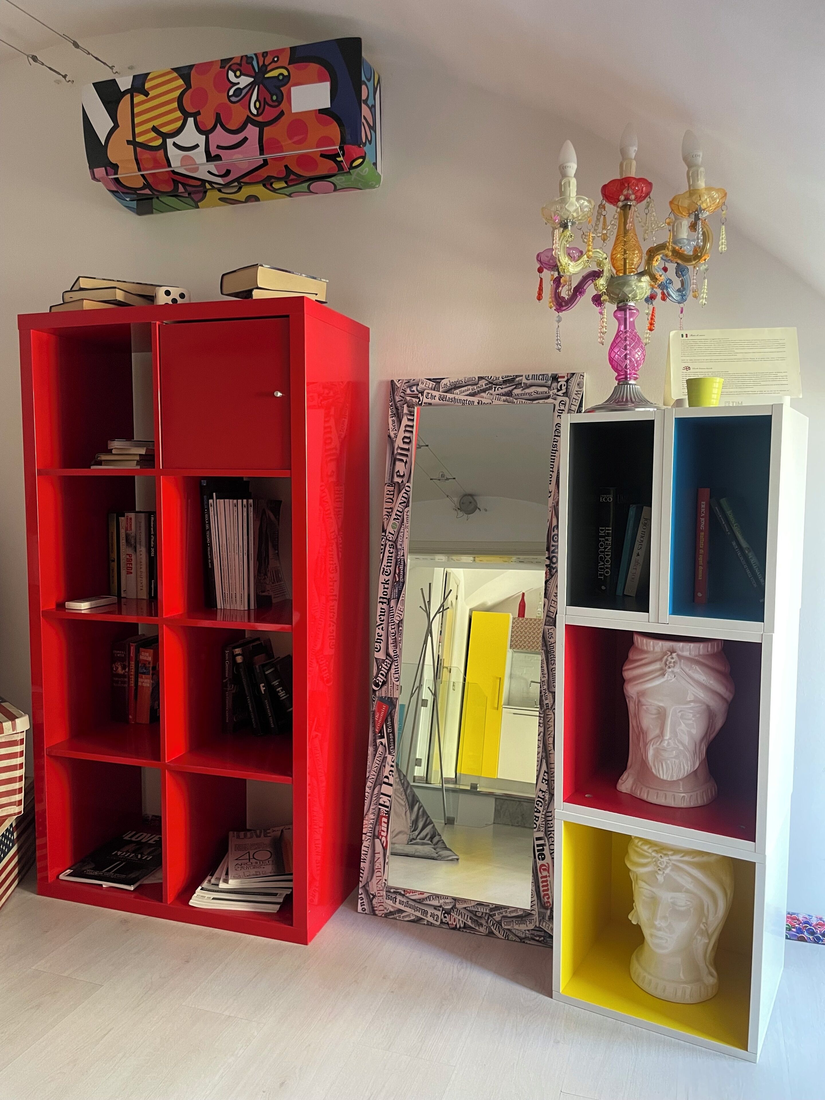 A room with a red bookshelf, a mirror with newspaper print, and a decorative candelabra.
