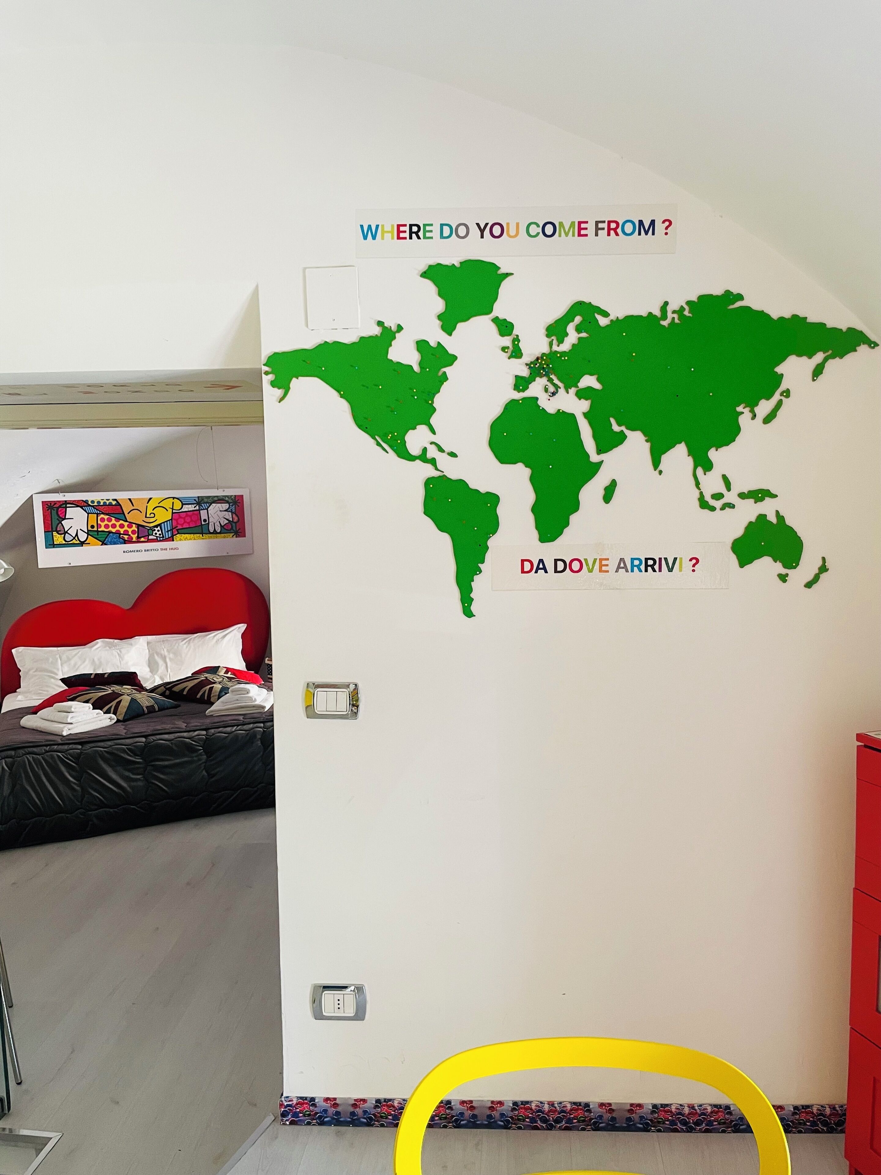 A bedroom with a bed, a red headboard, a world map wall decal, and a small table with a tray.