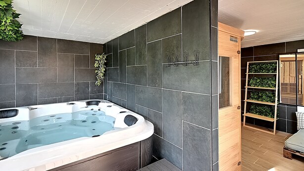 Ein modernes Badezimmer mit einer großen Badewanne, dunklen Fliesenwänden und einer hölzernen Sitzbank.