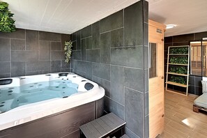 A modern bathroom with a large bathtub, dark tiled walls, and a wooden bench. - Le Chemin des Cerisiers - Maison vue montagne (Le Tholy)