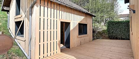 A wooden cabin with a tiled roof, a deck, and a small outdoor grill.