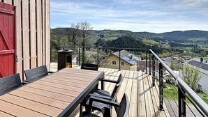 Eine Holzterrasse mit Tisch und Stühlen, mit Blick auf ein malerisches Tal mit Häusern und Hügeln.