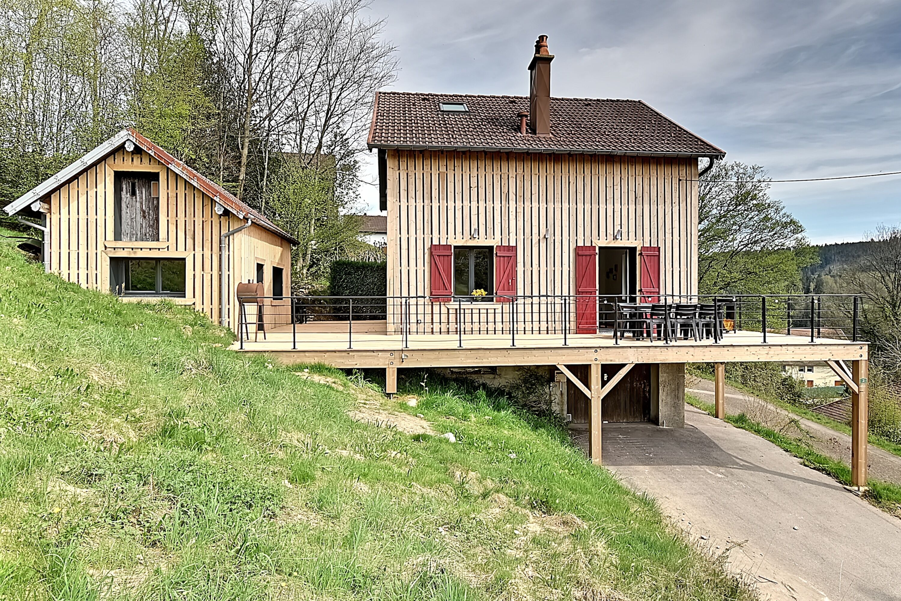 A two-story wooden house with a balcony, a chimney, and a small attached structure.