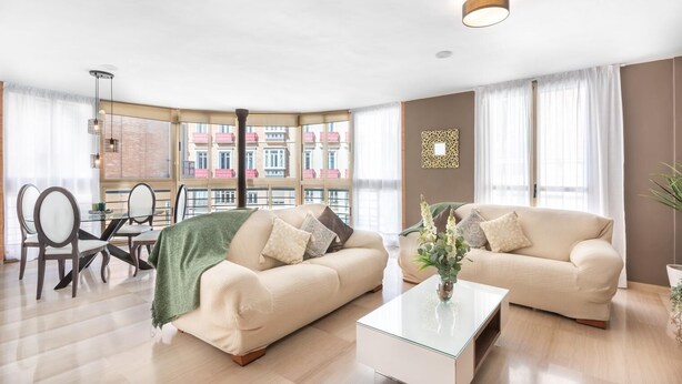 Ein modernes Wohnzimmer mit zwei Sofas, einem Glastisch und einem Essbereich mit Stühlen und Tisch.
