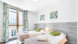 Ein modernes Schlafzimmer mit zwei Betten, einem Holzkopfende und einem Balkon mit tropischen Vorhängen.