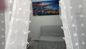 A bedroom with a bed, a painting of a cityscape, and a white curtain with a floral pattern. - Una Notte a Napoli (Naples)