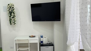 A small kitchenette with a fridge, a white table, and a chair. A flat-screen TV is mounted on the wall above the table. - Una Notte a Napoli (Naples)
