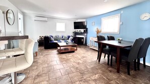 Un salon comprenant un canapé, une table basse, une table à manger avec des chaises, et un téléviseur fixé au mur.